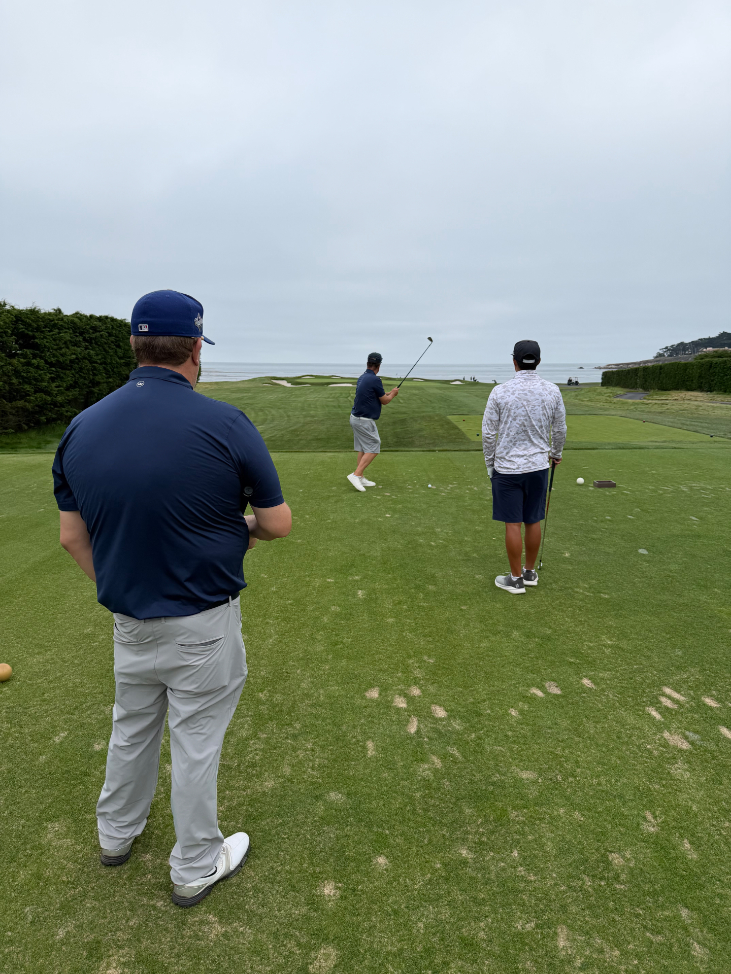 The family on the tee at Pebble Beach, one of them mid-swing toward the ocean